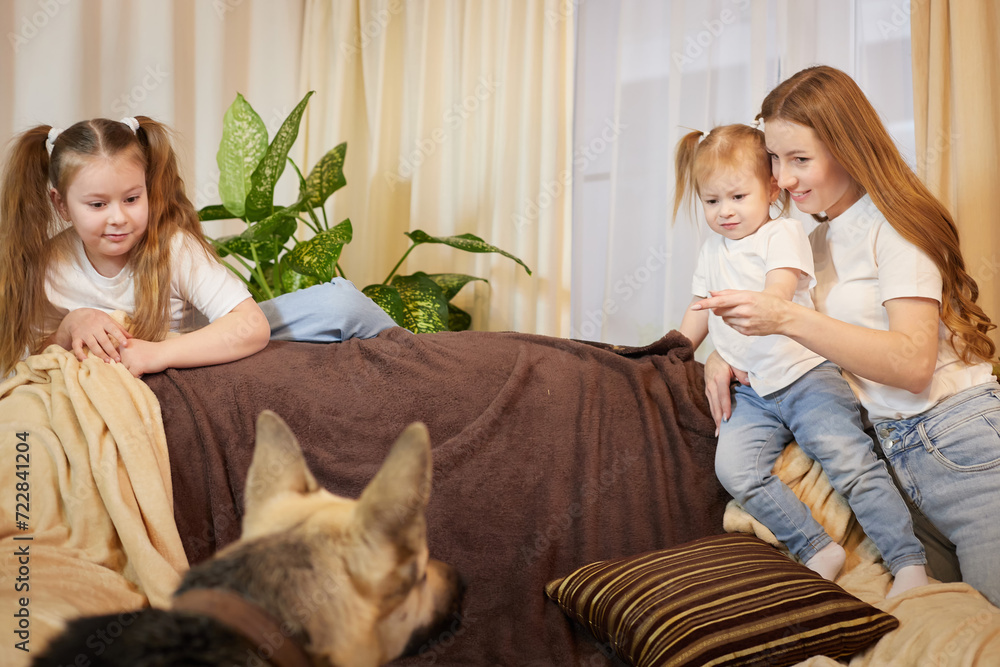 Loving family with mother, daughter sisters and big dog in living room. Woman mom, small child girl, female teenager who is afraid of a big pet Loving family with mother, daughter sisters and big dog in living room. Woman mom, small child girl, female teenager who is afraid of a big pet