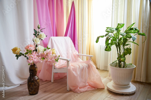 Delicate bright pink interior of the room with armchair  a vase with roses  draped curtains and a window. Location and background in the photo studio