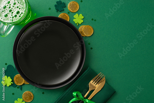 Enjoy St. Paddy's at the pub with a top-view shot of a table setting: black plate, folded napkin with knife and fork, beer glass, gold coins, trefoils, confetti on a vibrant green backdrop