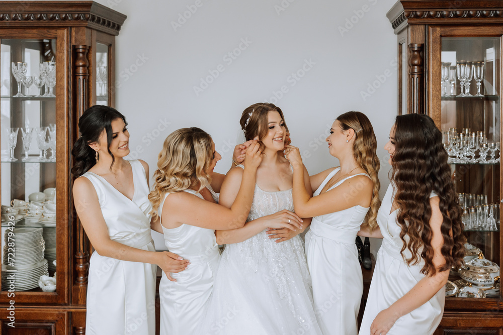 Wedding morning. Bridesmaids help put on the white wedding dress. A young woman is preparing to meet her groom and having fun with her friends Wedding morning. Bridesmaids help put on the white wedding dress. A young woman is preparing to meet her groom and having fun with her friends