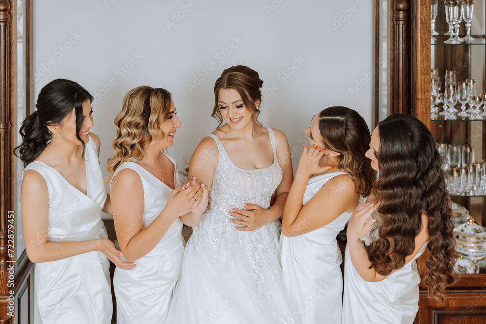 Wedding morning. Bridesmaids help put on the white wedding dress. A young woman is preparing to meet her groom and having fun with her friends Wedding morning. Bridesmaids help put on the white wedding dress. A young woman is preparing to meet her groom and having fun with her friends