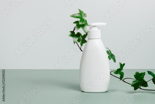 White cosmetic pump bottle for body lotion, shampoo or soap with green plant leaves on green background, copy space. Natural skincare, spa treatment. Template for beauty products, neutral aesthetics © Natureveryday
