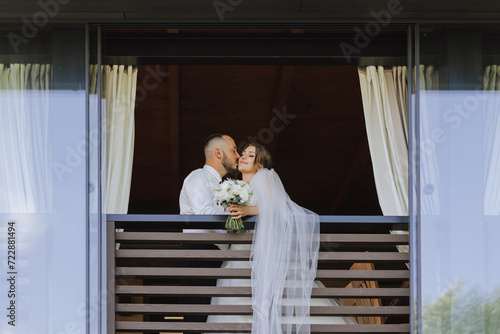 a newly married couple. the wind lifts a long white veil in summer. The bride and groom are hugging, a long veil is blowing in the wind. The newlyweds kiss on the balcony of the restaurant © Vasil
