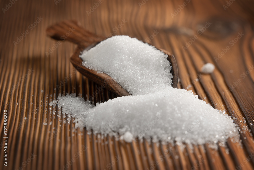 Close-up of granulated white sugar in a scoop on a wooden rustic background. Front view. Close-up of granulated white sugar in a scoop on a wooden rustic background. Front view.