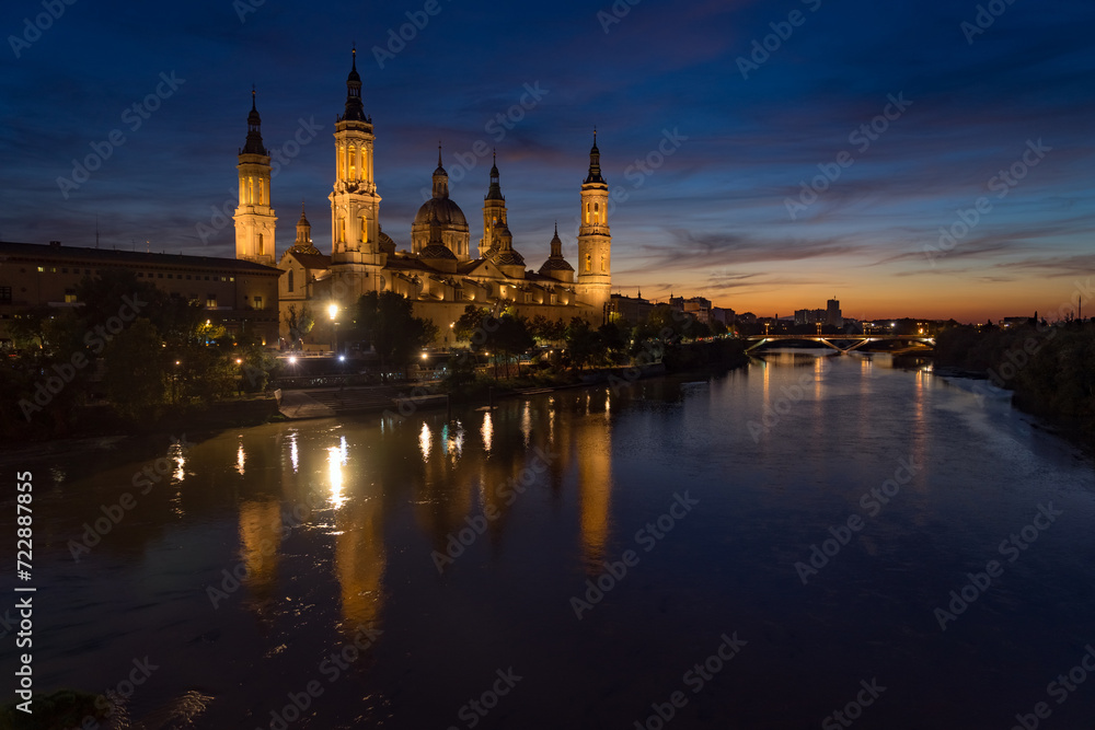 Pilar basilica of the city of Zaragoza reflected on the Ebro river at sunset with a dramatic sky. Aragon, Spain.