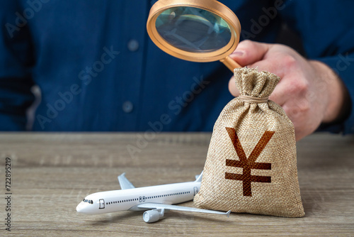 Airplane and chinese yuan or japanese yen money bag under investigation. Economic impact of aviation industry. Payment of taxes, fees and excise taxes. Measure impact on local economy. photo