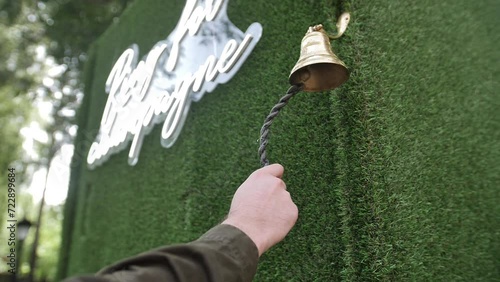 Decorative bell on chains outside on wall with grass decoration. Close-up of the ringing of a metal bell. photo