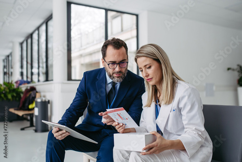 Pharmaceutical sales representative talking with doctor in medical building. Ambitious male sales representative presenting new medication on tablet.