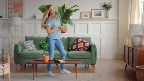 young blonde woman enter living room carrying green plants, put the on furnished for coziness and home staging, sits down to enjoy and rest