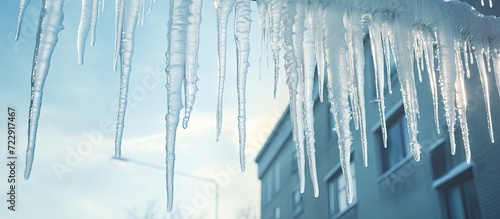 Huge icicles with sharp ends hang dangerously from the snow covered roof of a tall building in winter Spring thaw water drips from the icicles. Creative Banner. Copyspace image