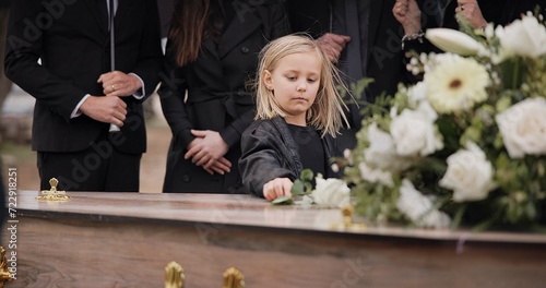 Fotografie Death, grief and girl at funeral with flower on coffin, family and sad child at service in graveyard for respect