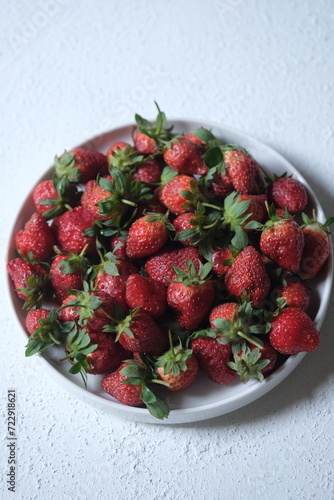 a pile of fresh strawberries on a white ceramic plate. Strawberry is a fruit that contains antioxidants and vitamin C. served on white table. 