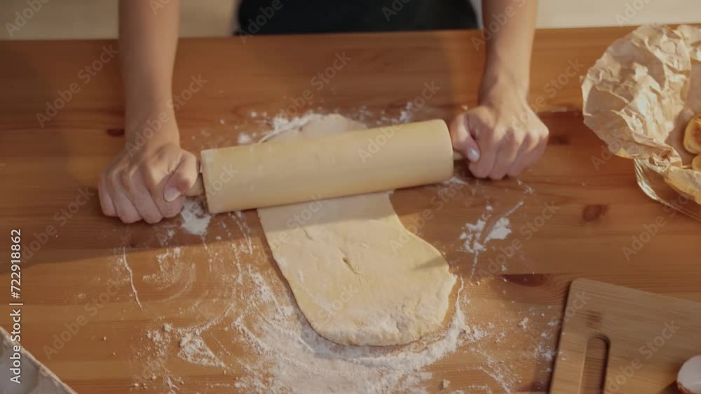 Womens hands roll out dough with a rolling pin on the kitchen table. Womens hands roll out dough with a rolling pin on the kitchen table.