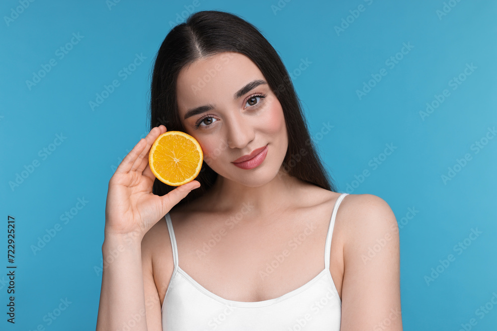 Beautiful young woman with piece of orange on light blue background Beautiful young woman with piece of orange on light blue background