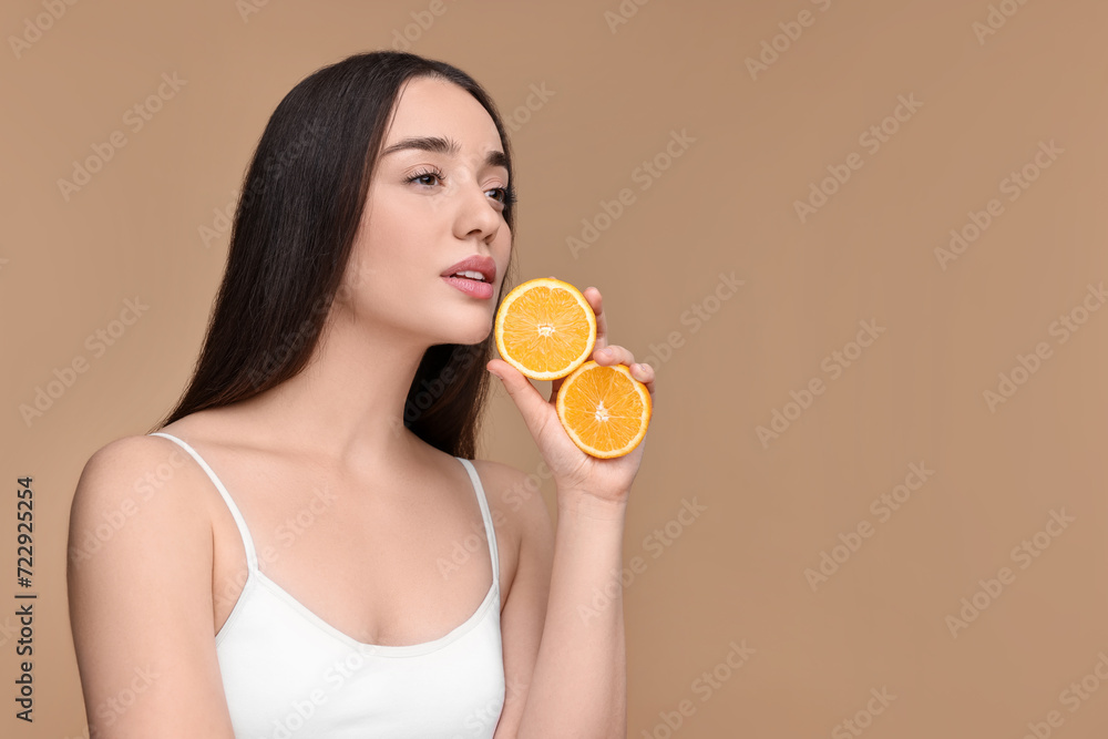 Beautiful young woman with pieces of orange on beige background. Space for text Beautiful young woman with pieces of orange on beige background. Space for text