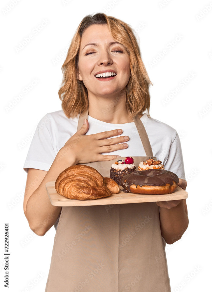 Middle-aged Caucasian woman baker with pastries laughs out loudly keeping hand on chest. Middle-aged Caucasian woman baker with pastries laughs out loudly keeping hand on chest.