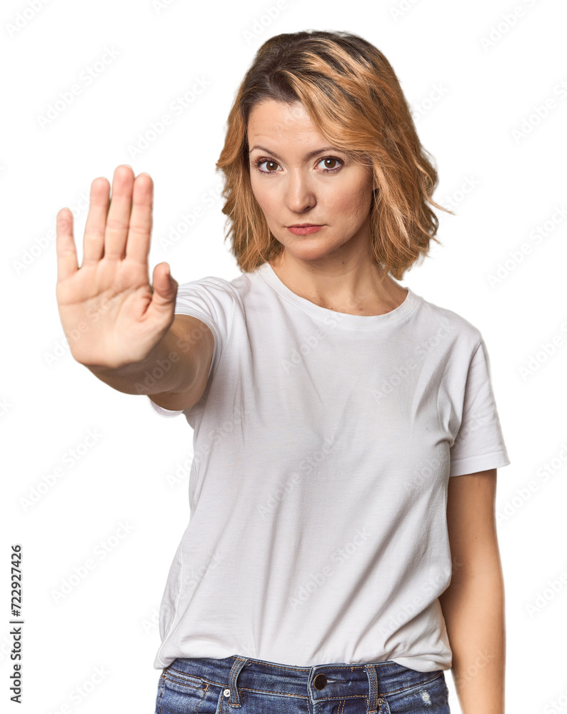 Fototapeta premium Blonde middle-aged Caucasian woman in studio standing with outstretched hand showing stop sign, preventing you.