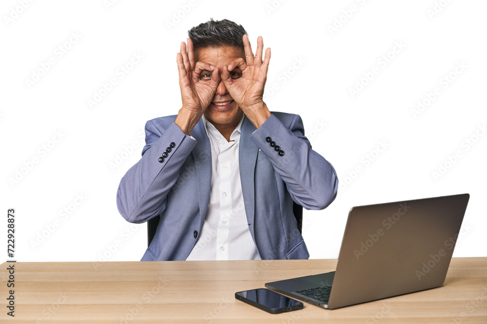 Elegant businessman at desk with laptop showing okay sign over eyes Elegant businessman at desk with laptop showing okay sign over eyes