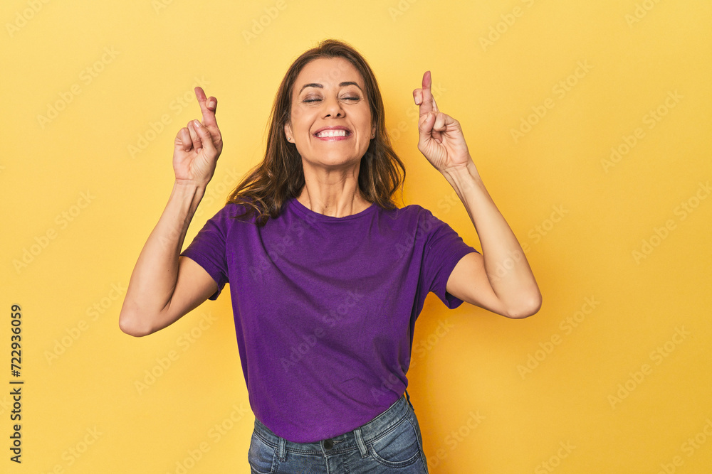 Middle-aged caucasian woman on yellow crossing fingers for having luck