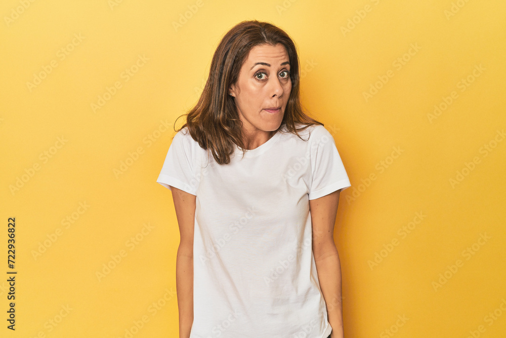 Middle-aged caucasian woman on yellow shrugs shoulders and open eyes confused. Middle-aged caucasian woman on yellow shrugs shoulders and open eyes confused.