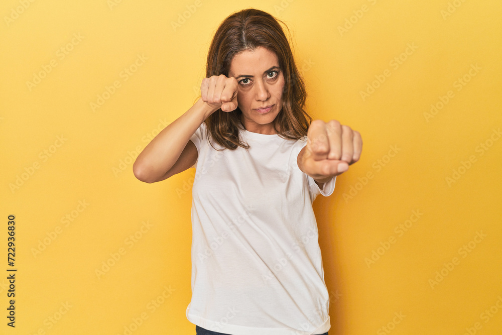Middle-aged caucasian woman on yellow throwing a punch, anger, fighting due to an argument, boxing. Middle-aged caucasian woman on yellow throwing a punch, anger, fighting due to an argument, boxing.