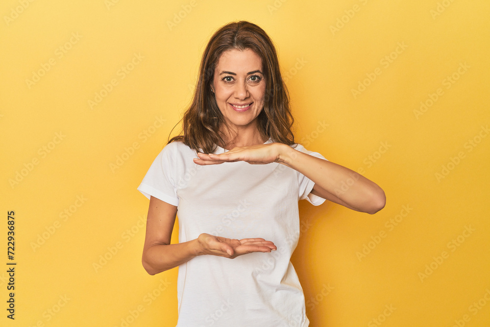 Obraz premium Middle-aged caucasian woman on yellow holding something with both hands, product presentation.