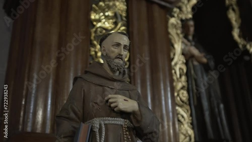 A statue of a Franciscan monk in contemplation, clad in a brown robe with a rosary, embodying spiritual devotion within a richly detailed wooden setting. photo