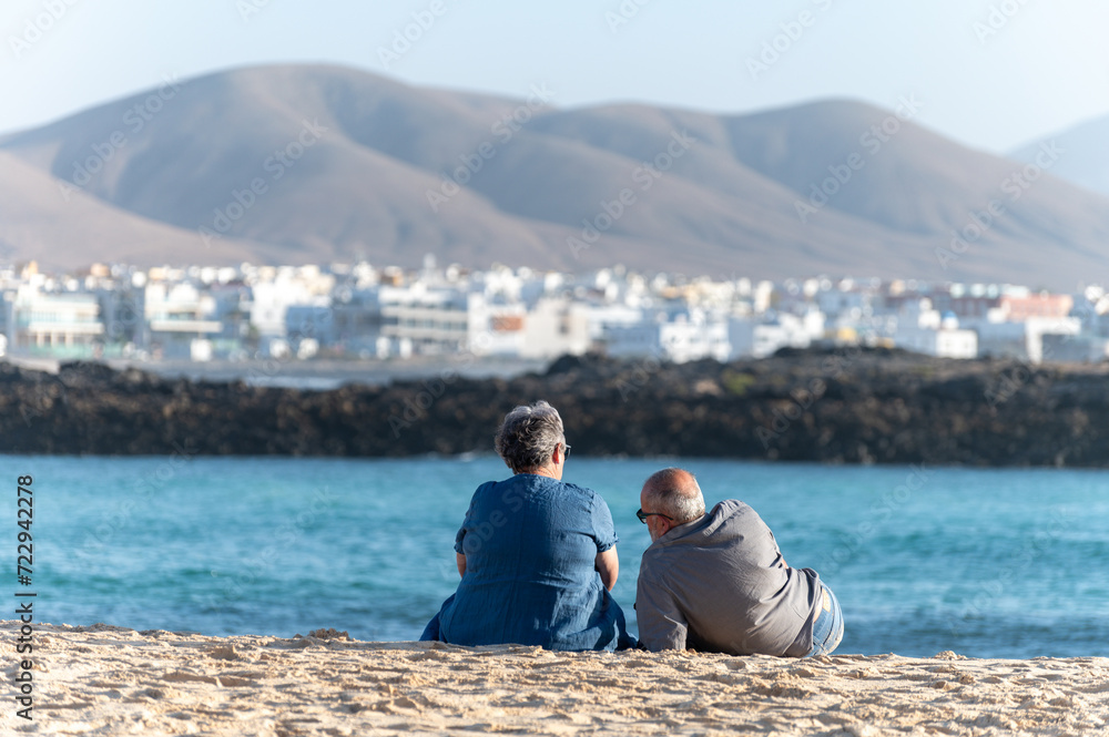 Fototapeta premium West coast of Fuerteventura island. Winter sea and sun vacation in El Cotillo touristic village, Canary islands, Spain. Unidenfitied old couple relaxing on white sandy beach La Concha..