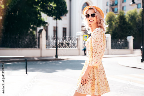 Young beautiful smiling blond woman in trendy summer yellow dress. Sexy carefree woman posing in the street at sunset. Positive model outdoors at sunny day. Cheerful and happy. In hat