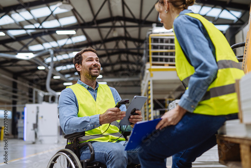 Portrait of man in wheelchair working in modern industrial factory, talking with female coworker. Concept of workers with disabilities, accessible workplace for employees with mobility impairment. photo