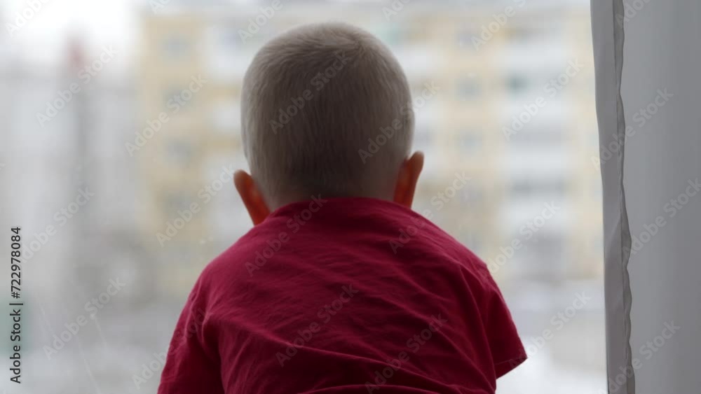 3-year-old child sitting by the window in winter, little boy looks out the window onto the street. 3-year-old child sitting by the window in winter, little boy looks out the window onto the street.