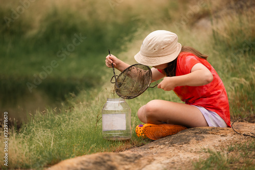 Girl catching tadpoles. Outdoor nature activity. photo