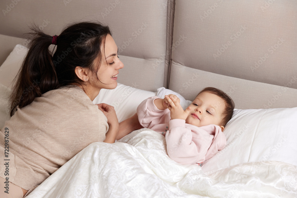 happy mother playing with her cute baby daughter on bed in bedroom. loving family having fun happy mother playing with her cute baby daughter on bed in bedroom. loving family having fun
