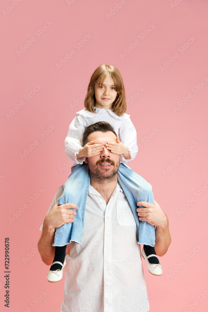 Joy of fatherhood. Little girl sitting on man's shoulders and covered his eyes with palms against pink pastel background. Concept of International Day of Happiness, childhood and parenthood. Ad Joy of fatherhood. Little girl sitting on man's shoulders and covered his eyes with palms against pink pastel background. Concept of International Day of Happiness, childhood and parenthood. Ad
