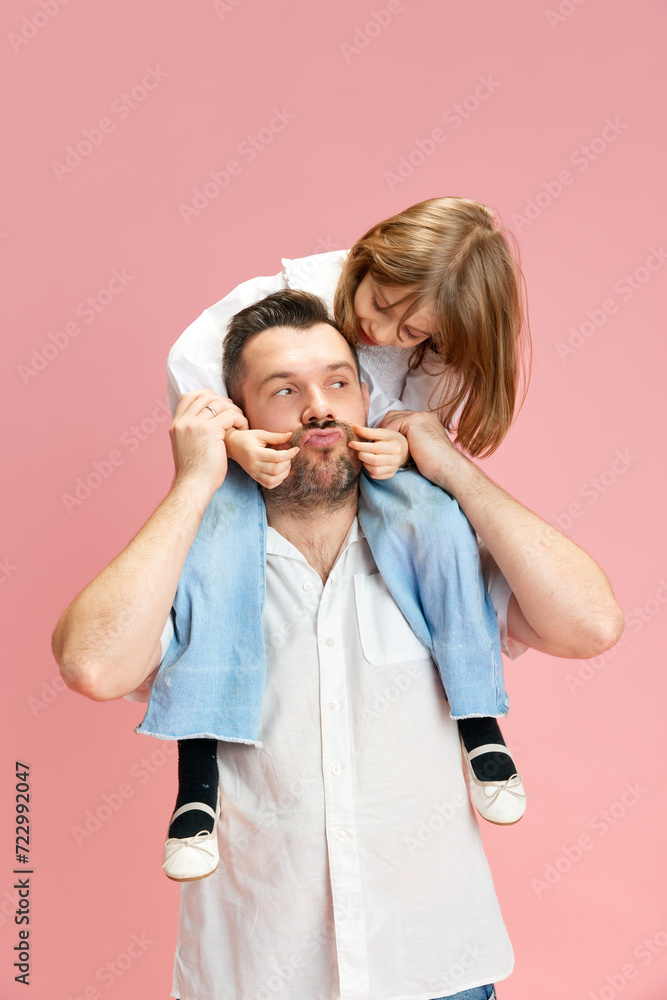 Father with daughter on shoulders who plays with daddy's' moustaches against pink pastel background. Concept of International Day of Happiness, childhood and parenthood, positive emotions. Ad Father with daughter on shoulders who plays with daddy's' moustaches against pink pastel background. Concept of International Day of Happiness, childhood and parenthood, positive emotions. Ad