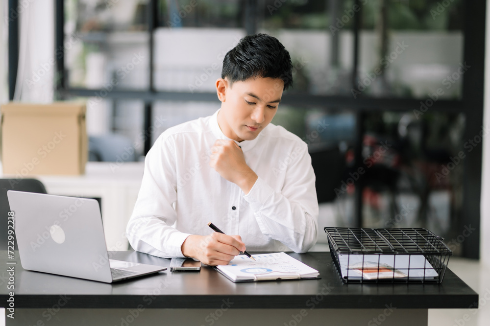 Young handsome man typing on tablet and laptop while sitting at the working tabl in office. Young handsome man typing on tablet and laptop while sitting at the working tabl in office.