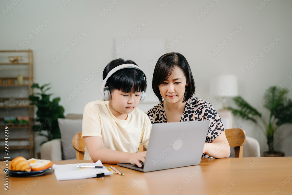 Homeschool Asian young little boy learning online and does homework by using computer and tablet with mother help, teach and encourage. son smile to study at home together with mom Homeschool Asian young little boy learning online and does homework by using computer and tablet with mother help, teach and encourage. son smile to study at home together with mom