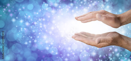 Reiki Remote Healing Template Background - Male Reiki Master Healer with parallel hands reaching into white light against wide beautiful blue bokeh background and copy space for spiritual message 