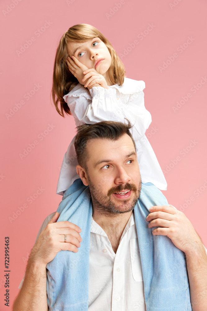 Pensive child on father's shoulders, both in contemplation against pink pastel background. Concept of International Day of Happiness, childhood and parenthood, positive emotions. Ad