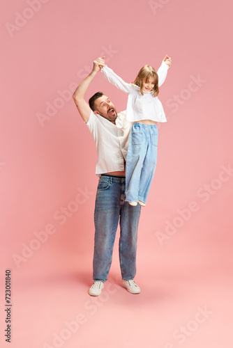 Dad and me. Full length portrait of Man holding up child with raised arms against pink pastel background. Concept of International Day of Happiness, childhood and parenthood, positive emotions. Ad