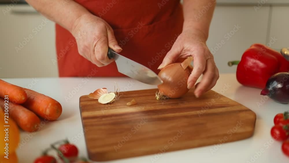Female chef is precisely slicing fresh onions on wooden board while preparing italian pasta with vegetables and soup in kitchen