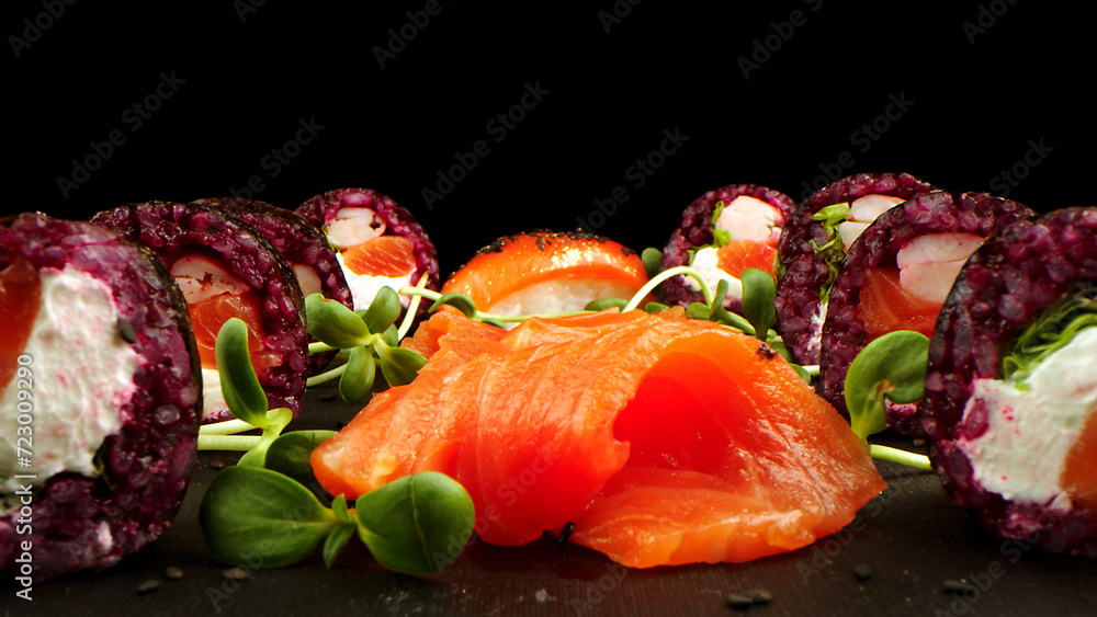 Variety of bright sushi rolls with greens on a black background. Incredible fresh sushi rolls on a dark background. Cooking traditional Japanese seafood and fish dishes. Variety of bright sushi rolls with greens on a black background. Incredible fresh sushi rolls on a dark background. Cooking traditional Japanese seafood and fish dishes.