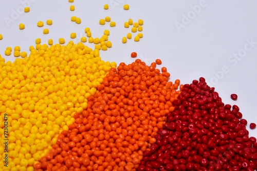 Yellow, orange and red masterbatch granules on a white background, this polymer is a coloring agent for products in the plastics industry