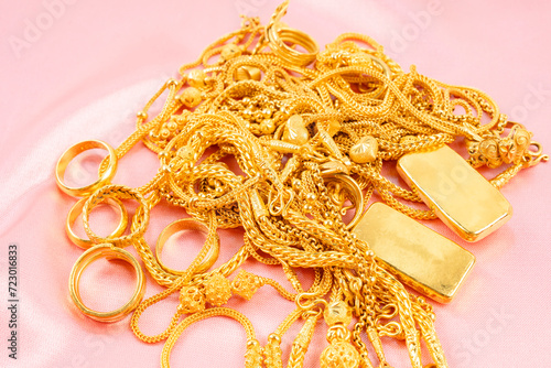 Many gold necklaces and gold bars on pink fabric background.