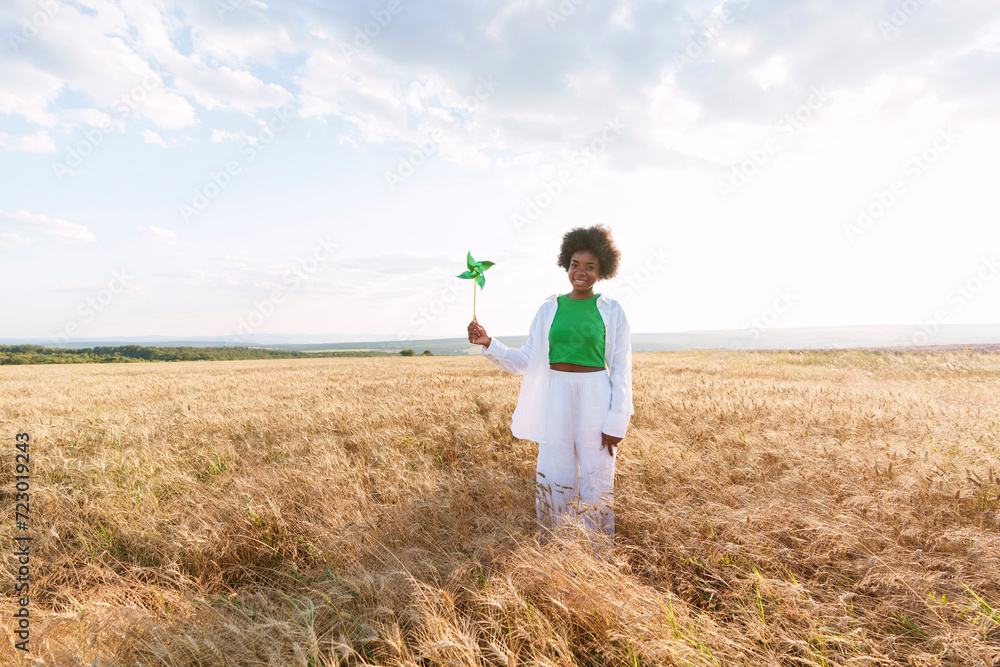 Smiling woman holding pinwheel toy standing amidst plants in field Smiling woman holding pinwheel toy standing amidst plants in field
