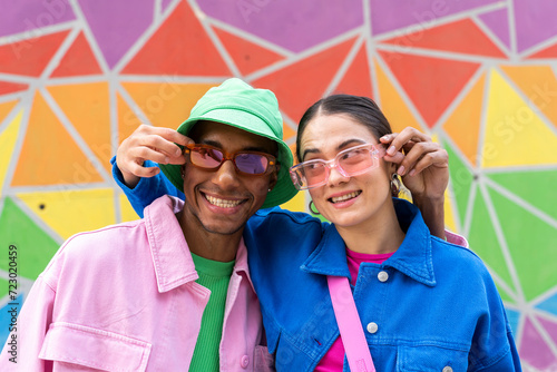 Smiling couple holding sunglasses in front of colorful wall photo