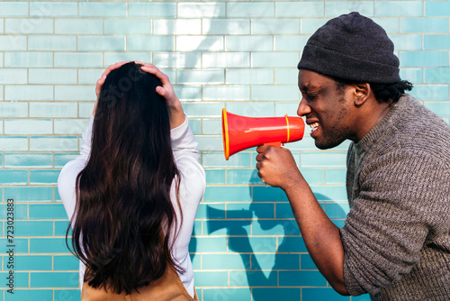 Angry man shouting through megaphone on woman with head in hands facing wall photo