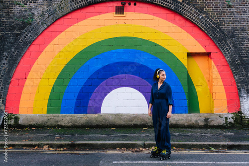 Woman wearing wireless headphones and roller skates in front of rainbow wall photo