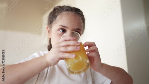 girl child drinking juice. happy family a healthy eating kid dream concept. daughter girl drinking yellow juice from a glass cup in the kitchen indoors. child drinking fruit juice