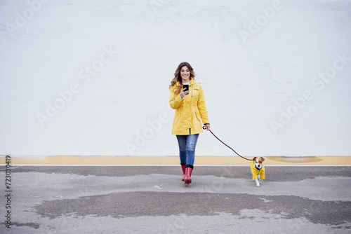 Young woman using smart phone and walking with dog on road